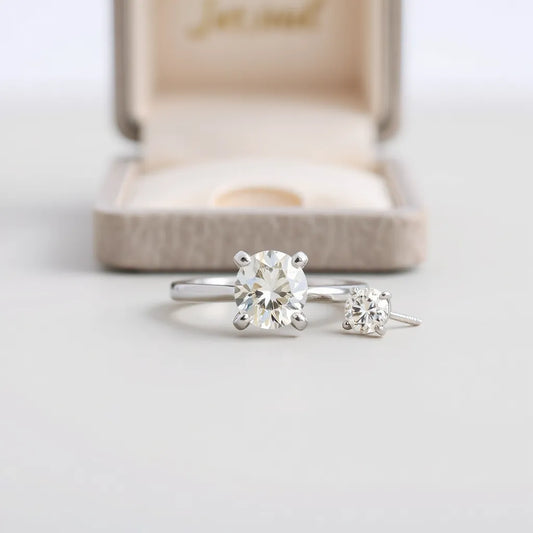 Moissanite ring and matching stud earrings with a clearly faceted stone on a neutral background